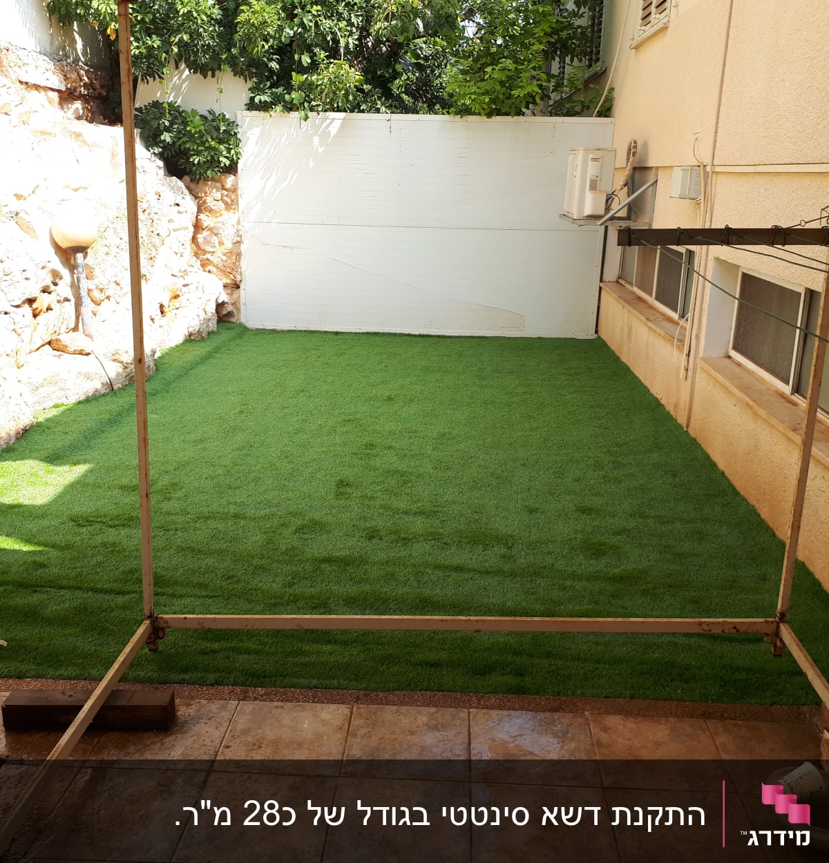 דשא סינתטי בחצר קטנה עם קיר אבן ועצים